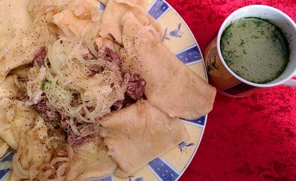 Teller mit der traditionelle Kasachstanische Speise Beshbarmak: Teigtaschen mit Fleisch und Zwiebeln und separate Tasse mit der Brühe