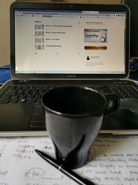 Dunkelblaue Tasse auf einem Heft vor dem Laptop 