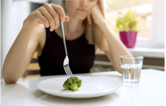Frau mit Gabel und einem Stück Broccoli auf dem weißen Teller